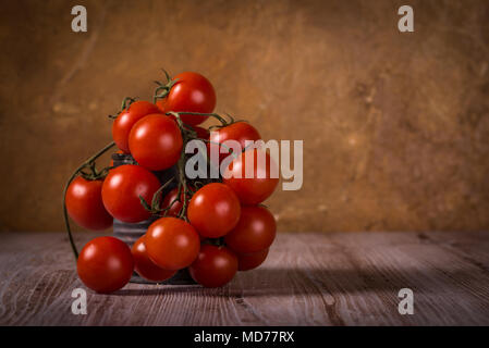 Horizontale Foto mit wenigen Zweige voller kleiner roter Kirsche Tomaten. Gemüse in Vintage getragen werden kann. Zinn ist auf Holzbrett mit weißen und braue Stockfoto