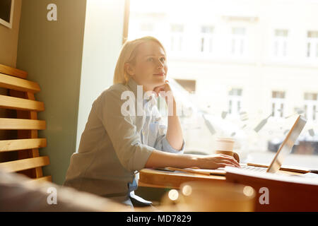 Junge nachdenklich Geschäftsfrau, Kaffee zu trinken und mit Laptop im Cafe Stockfoto