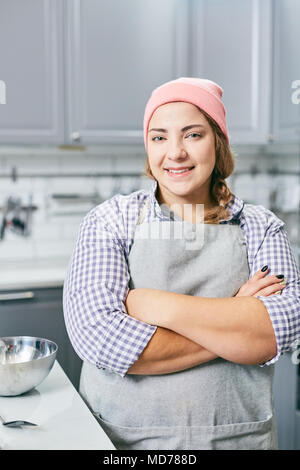 Porträt der jungen kaukasischen Frauen kochen Sie in der Schürze in der Küche und ihre Hände gekreuzt und lächelnd an Kamera Stockfoto