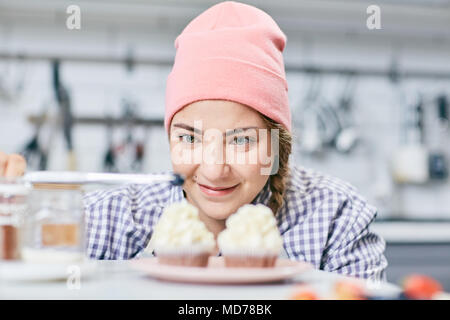 Junge weibliche Konditor in rosa Hut verzieren cream Cupcakes mit Blaubeeren auf unscharfen Hintergrund Stockfoto