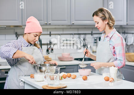 Professionelle weiblichen Konditoren Eier rühren und Sieben Mehl durch Sieb während der Kuchen in der modernen Küche Stockfoto