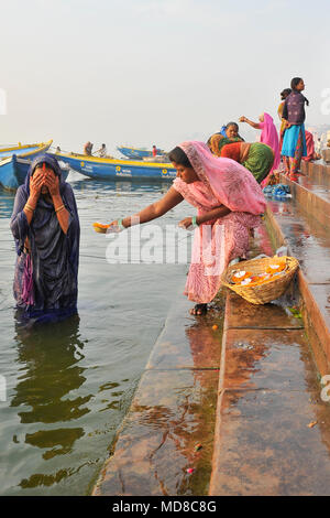 Eine Frau bietet Papier diyas für den Verkauf an eine Frau baden in den Ganges Stockfoto