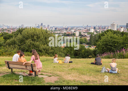 Drei junge Frauen sitzen auf einer Bank mit Blick auf die Skyline von London an einem Sommernachmittag auf dem Parliament Hill in Hampstead Heath in London Stockfoto