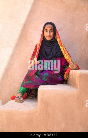 Nizwa, Oman - Mar 24, 2018: Portrait eines schönen jungen omanischen Mädchen mit einem orangefarbenen Schal sitzt auf einem Fort schritte. Stockfoto