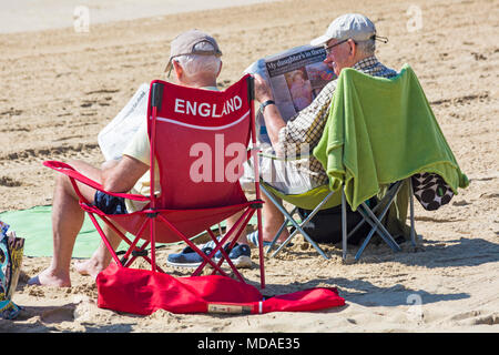 Bournemouth, Dorset, Großbritannien. 19. April 2018. UK Wetter: schön warmen sonnigen Tag in Bournemouth Stränden mit klarem blauen Himmel und Sonnenschein, ungebrochen als Besucher der seaside Leiter der wärmste Tag des Jahres so weit zu genießen. Zwei Männer Zeitung lesen am Strand, eine Sitzung auf England Stuhl. Credit: Carolyn Jenkins/Alamy leben Nachrichten Stockfoto