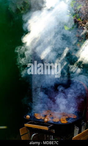 Lichtstrahlen, die durch dicken Rauch über Schweinefleisch Steaks auf dem Holzkohlegrill Stockfoto