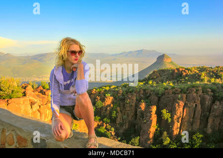 Jungen Touristen sitzen auf den Felsen bei Sonnenuntergang nach dem Trekking im Tal der Verwüstung in der Nähe von Graaff-Reinet, Südafrika. Blonde Frau mit Luftaufnahmen, Camdeboo National Park, Karoo, Eastern Cape. Stockfoto