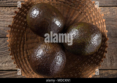 Avocado in Weidenkorb auf einer hölzernen Hintergrund Stockfoto