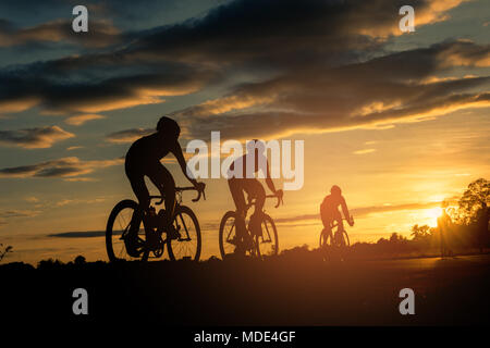 Die Männer fahren Fahrräder bei Sonnenuntergang mit orange-blauer Himmel. Abstrakte Silhouette Hintergrund Konzept. Stockfoto