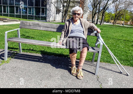 Eine ältere Dame, die auf einer Parkbank sitzt, eine alte Bank, eine Seniorin allein Stockfoto