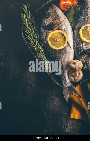 Blick von oben auf die Fisch mit Gemüse und Gewürze in Backform auf unebenem Untergrund. Stockfoto