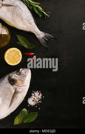 Blick von oben auf die dorado Fisch und verschiedenen Gewürzen auf dunklen rauen Tabelle. Stockfoto