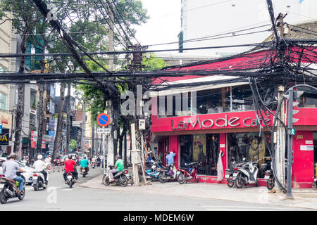 Ein Gewirr von elektrischen Freileitungen und Telefon Kabel an einer belebten Kreuzung mit Verkehr von Motorrädern in Ho Chi Minh City, Vietnam. Stockfoto