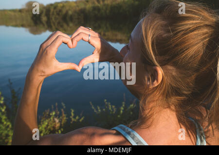 Junge Frau von der Seepromenade, die Form eines Herzens finger Rahmen auf schöne Landschaft, Reflexion über die Wasseroberfläche. Die Menschen reisen Liebe Umwelt Stockfoto