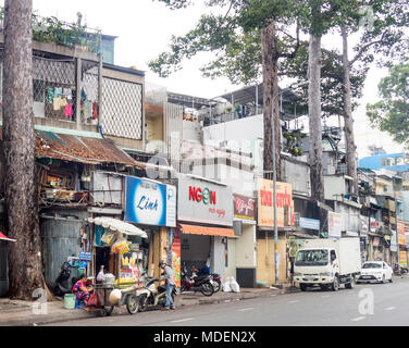 Straßenbild aus einer Reihe von Geschäftshäusern und Street Food Anbieter auf einer von Bäumen gesäumten Straße in Ho Chi Minh City, Vietnam. Stockfoto