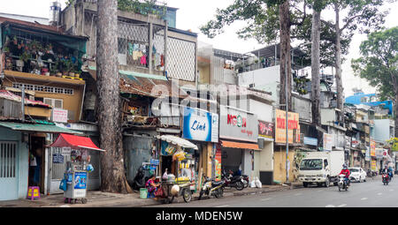 Straßenbild aus einer Reihe von Geschäftshäusern und Street Food Anbieter auf einer von Bäumen gesäumten Straße in Ho Chi Minh City, Vietnam. Stockfoto