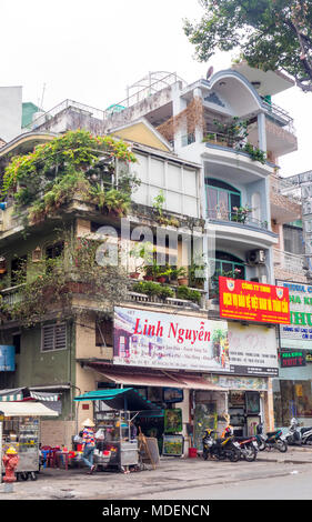 Straßenbild aus einer Reihe von Geschäftshäusern und Street Food Anbieter auf einer von Bäumen gesäumten Straße in Ho Chi Minh City, Vietnam. Stockfoto