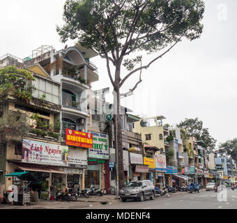 Straßenbild aus einer Reihe von Geschäftshäusern und Street Food Anbieter auf einer von Bäumen gesäumten Straße in Ho Chi Minh City, Vietnam. Stockfoto