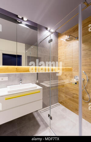 Modernes Badezimmer mit Glasduschkabine, dunklen grauen Fliesen, Spiegel und weißen Waschbecken Stockfoto