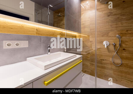 Interieur aus Holz und Marmor Badezimmer mit Glastür, Edelstahl Duschkopf und weißen Schränke Stockfoto