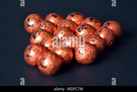 Orange Kürbis verpackte Pralinen in einer Reihe, auf einem schwarzen Hintergrund. Nahaufnahme von Halloween Jack-o-Lantern Folie überzogen Süßigkeiten. Bereit für Tric zur Hand Stockfoto