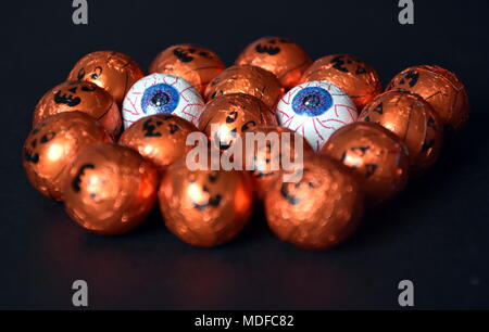 Orange Kürbis verpackte Pralinen in einer Reihe, auf einem schwarzen Hintergrund. Nahaufnahme von Halloween Jack-o-Lantern Folie überzogen Süßigkeiten. Bereit für Tric zur Hand Stockfoto