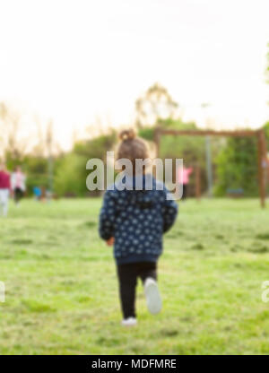 Unscharf geschossen. Kleines Mädchen von hinten im Park spielen mit anderen Kindern. Stockfoto