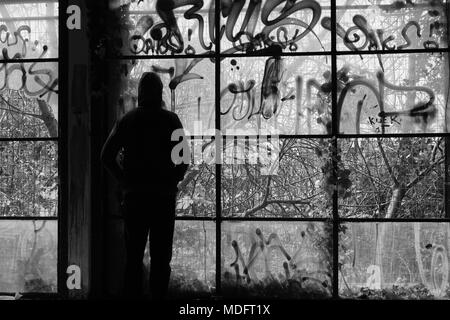 Mann gegen Glaswand zerbrochene Fenster in verlassenen Gebäude. Schwarz und Weiß. Stockfoto