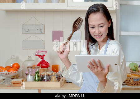 Asiatische Frau ist Kochen in der Küche mit digitalen Tablette der Rezeptur. Stockfoto
