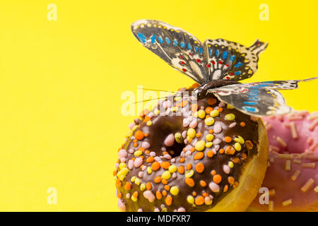 Sie sprengten Rosa und chokolate Donut. Frosted sprengte Donuts mit Schmetterling auf gelben Hintergrund. Kopieren Sie Raum auf der linken Seite Stockfoto