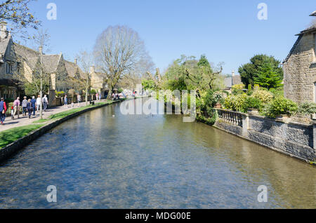 Touristen am Ufer des Flusses Windrush im beliebten Cotswold Dorf Bourton-on-the-Water, Gloucestershire in der Frühlingssonne Stockfoto