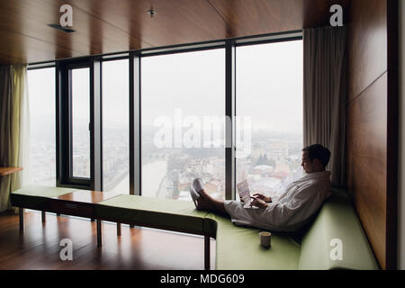 Attraktiver Mann in seinem Kaffee am Morgen auf seinem Computer in seinem Hotel Zimmer Stockfoto