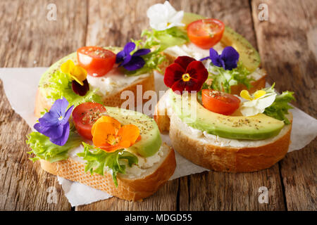 Sandwiches mit essbaren Blumen, frische Avocado- und Frischkäse close-up auf dem Tisch. Horizontale Stockfoto