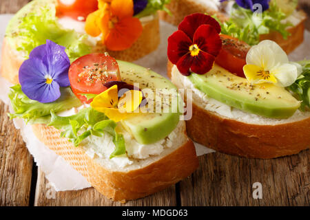 Festliche Toasts mit Avocado, Tomaten, essbare Blüten und Frischkäse close-up auf dem Tisch. Horizontale Stockfoto