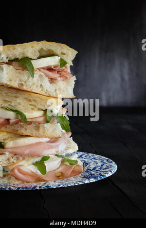 Sandwich mit weißen Pizza, Mortadella, Mozzarella, und Rucola auf schwarzem Hintergrund. Stockfoto