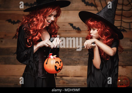 Halloween Konzept - Schönen weißen Mutter und ihre Tochter mit langen roten Haaren in Hexe Kostüme mit Halloween Candy und Zauberstab. Stockfoto