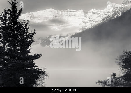 Silhouette eines Fotografen am Ufer des Lake Louise mit Nebel steigt aus dem See bei Sonnenaufgang, Banff National Park; Lake Louise, Alberta, Kanada Stockfoto