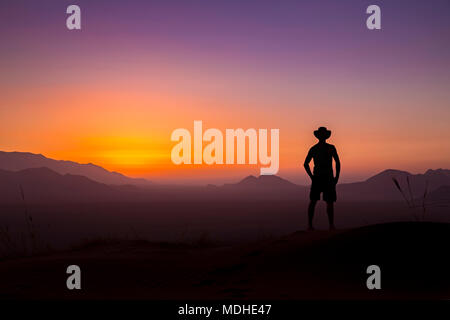 Silhouette der Mann mit dem Cowboyhut aus steht ein Blick auf die glühende Landschaft und Himmel bei Sonnenuntergang; Sossusvlei, Otjozondjupa Region, Namibia Stockfoto