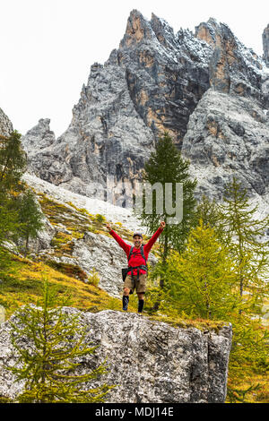 Männliche Wanderer mit Arme oben auf großen Felsen mit felsigen Hang und Berg; Sesto, Bozen, Italien Stockfoto