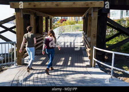 Zwei junge Frauen gehen gemeinsam auf einen Weg unter einer Brücke in einem Park; New Westminster, British Columbia, Kanada Stockfoto