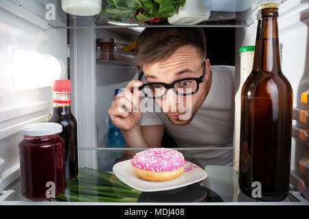 Mann entdeckt einen Donut im Kühlschrank. Stockfoto