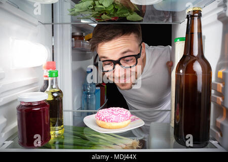 Nerd glücklich über einen Donut im Kühlschrank. Stockfoto