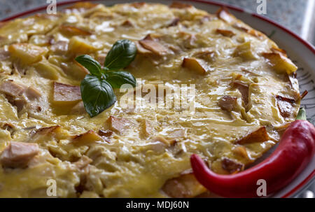 Frische Omelette mit Schinken und Kartoffeln auf dem Teller mit grünem Basilikum und heißen roten Pfeffer Stockfoto