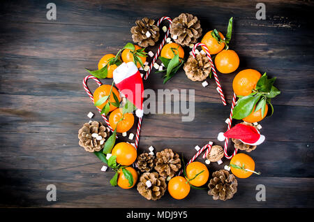 Mandarinen mit grünen Blättern, Weihnachten Spielzeug und Tannenzapfen in Form eines Kranzes auf dunklen alten Holztisch., kopieren Raum. top View Stockfoto