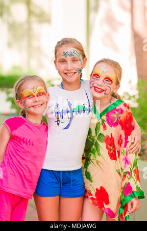 Glückliche kleine Mädchen mit Face Art malen im Park. Geburtstag des Kindes masquerade Party, Freunde, Spaß haben, Lachen und umarmten einander. Unterhaltung Stockfoto