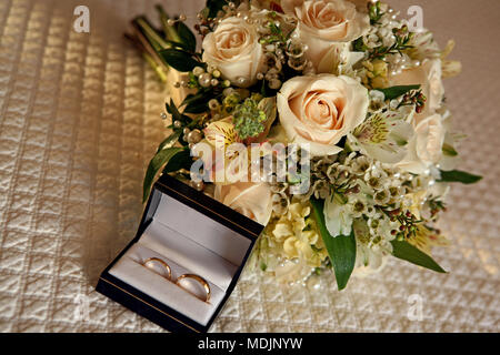 Schönen pfirsich Rosen wedding bouquet Sitzen auf einem Bett mit der Hochzeit Ringe in das Feld Stockfoto