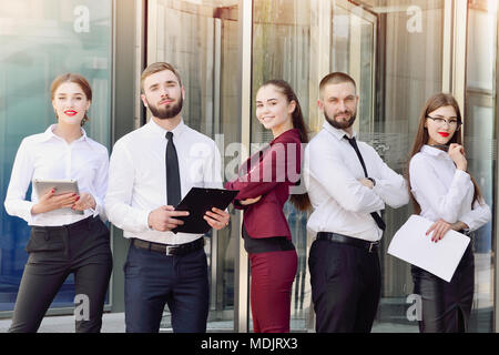 Befehl. Junge Berufstätige auf dem Hintergrund eines mehrstöckigen Gebäude aus Glas. Fünf Manager. Teamarbeit. Büro. Eine Gruppe von Menschen. Börsenhändler Stockfoto