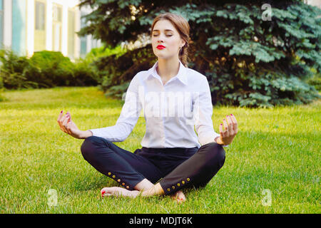 Büro Yoga. Business Lady im Lotussitz sitzt auf grünem Gras. Freizeit der Mitarbeiter des Amtes. Gesunde Lebensweise. Stockfoto