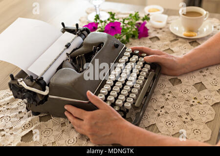 Schreiben Arbeitsplatz. Weibliche Hände halten retro Schreibmaschine auf Spitze Tischplatte platziert. Stockfoto