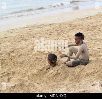 Jungen, die sich gegenseitig mit Sand am Strand Stockfoto